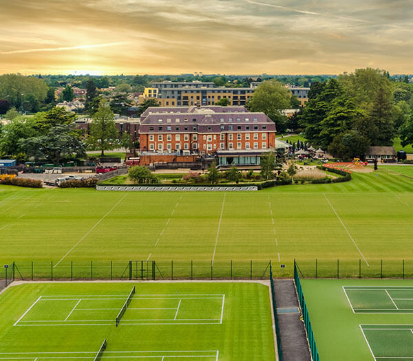Aerial view of Lensbury Resort with tennis courts and a hotel building set against a sunset sky.