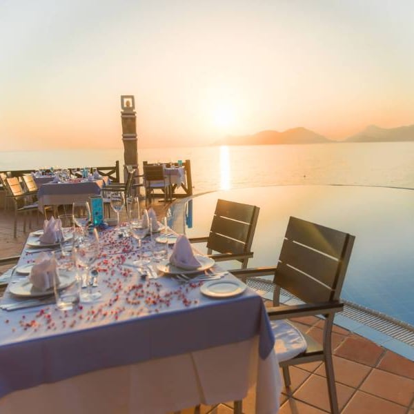 Dining table at Liberty Lykia Family Resort with sunset view over the sea and a poolside setting, showcasing elegant table settings.