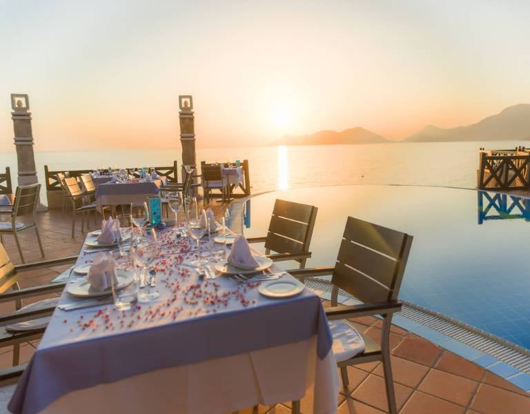 Dining table at Liberty Lykia Family Resort with sunset view over the sea and a poolside setting, showcasing elegant table settings.