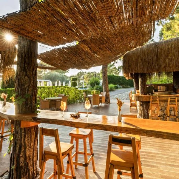 Outdoor bar at Liberty Lykia with wooden stools and bar, surrounded by greenery with woven shaded areas.