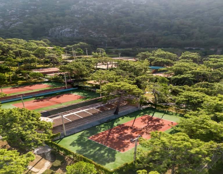 Drone view of Liberty Lykia Tennis Courts surrounded by trees and hills, showcasing a serene forest location.