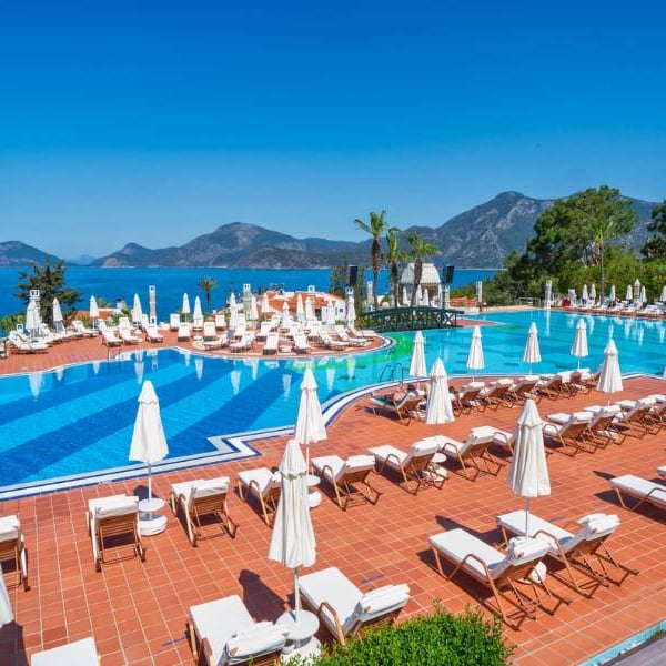 Liberty Lykia resort swimming pool with sun loungers and parasols, overlooking the sea and mountains.