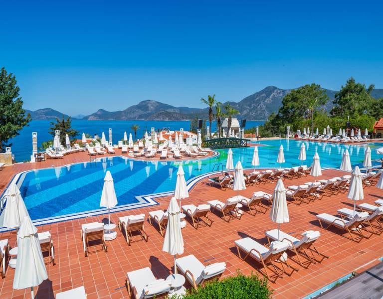 Liberty Lykia resort swimming pool with sun loungers and parasols, overlooking the sea and mountains.