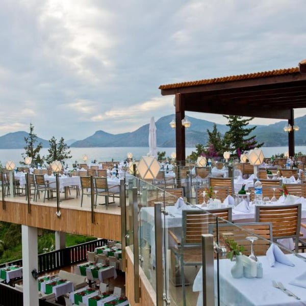 Liberty Lykia rooftop restaurant with sea and mountain views, featuring white tablecloths and wooden seating under a pergola.