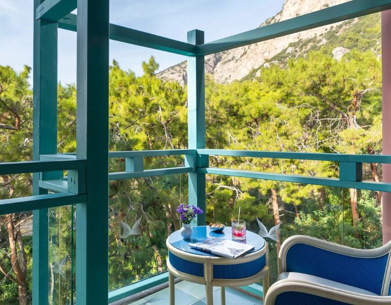Balcony at Liberty Lykia featuring a table with drinks, a plant, and views of green trees and mountains.