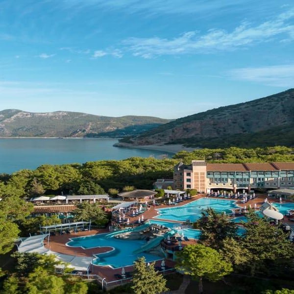 Aerial view of Liberty Sentido Gallery resort, highlighting the pool area, surrounding greenery, and bay with mountains in the background.