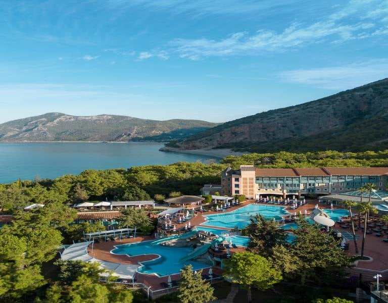 Aerial view of Liberty Sentido Gallery resort, highlighting the pool area, surrounding greenery, and bay with mountains in the background.