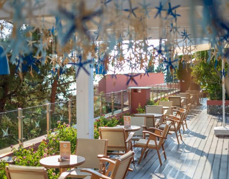 Outdoor terrace at Liberty Sentido Gallery Restaurant with wooden chairs, green plants, and star decorations.