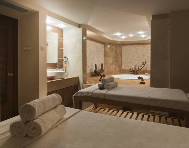Serene spa room at Liberty Sentido Gallery with massage tables, fresh towels, and a jacuzzi surrounded by rose petals.