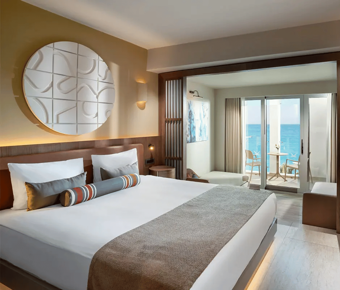 Luxurious hotel room at Liberty Village with a large bed, modern decor, and a balcony overlooking the sea.