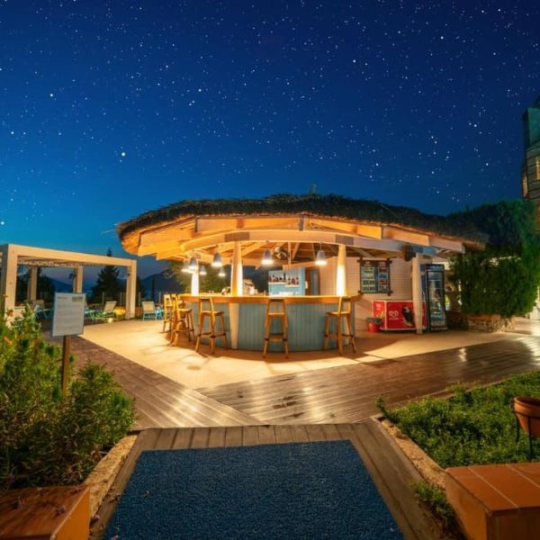 Night bar at Liberty Village Gallery with a round thatched roof, wooden stools, surrounded by greenery, and a star-filled sky.