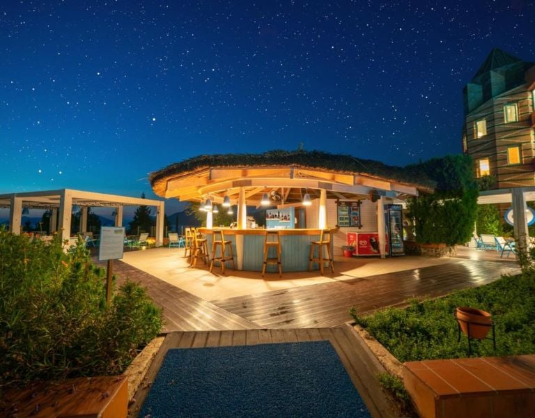 Night bar at Liberty Village Gallery with a round thatched roof, wooden stools, surrounded by greenery, and a star-filled sky.