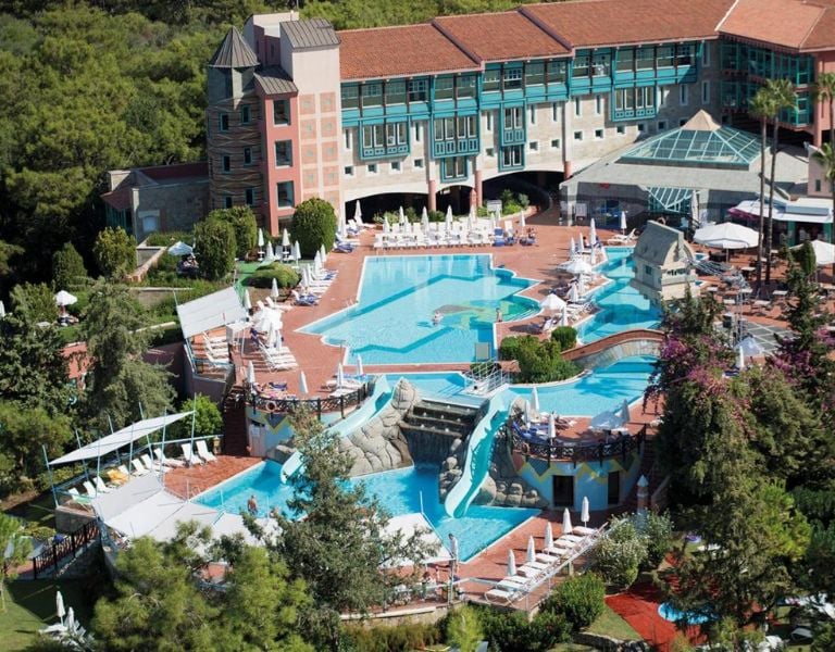 Aerial view of a luxury resort with a uniquely shaped outdoor pool, surrounded by lounge chairs and lush greenery.