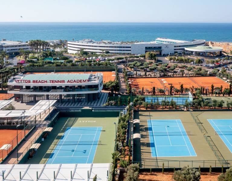 Aerial view of Lyttos Beach Tennis Academy with clay and hard courts near the Mediterranean Sea.