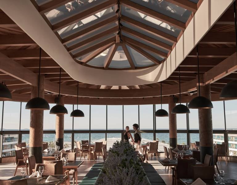 Interior of Lyttos Gallery Restaurant with wooden beams, pendant lights, and sea-view windows.