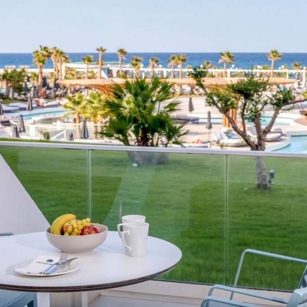 Lyttos Mare Resort balcony view with table and chairs, overlooking the pool, gardens, and sea.