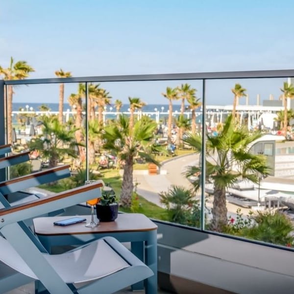 Balcony view from Lyttos Mare Resort with chairs, table, palm trees, pool, and sea.