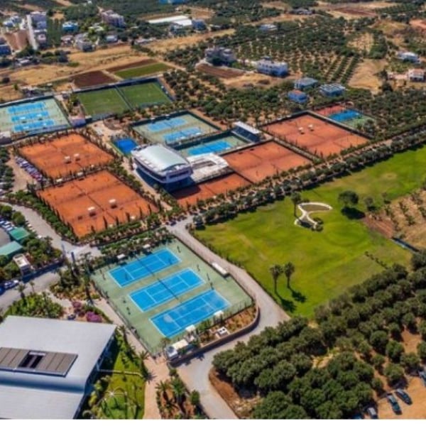 Aerial view of the Lyttos Mare tennis complex with multiple clay and hard tennis courts, olive groves, and a central building.