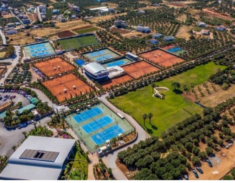Aerial view of Lyttos Mare's tennis courts, featuring several clay and hard surfaces in a green setting.