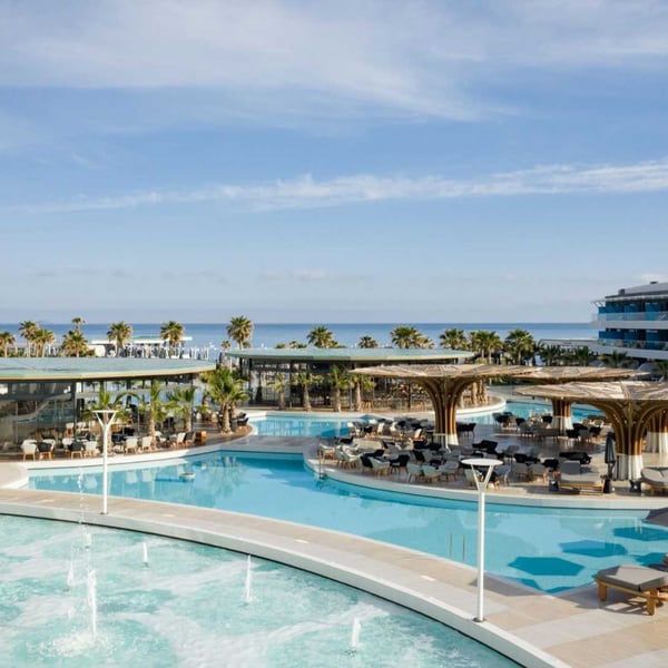 Lyttos Mare resort with luxurious turquoise pools, sun loungers, palm trees, and a sea view in the background.