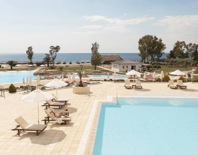 Meliton Gallery poolside with two swimming pools, sun loungers, umbrellas, and a view of the beach and sea.