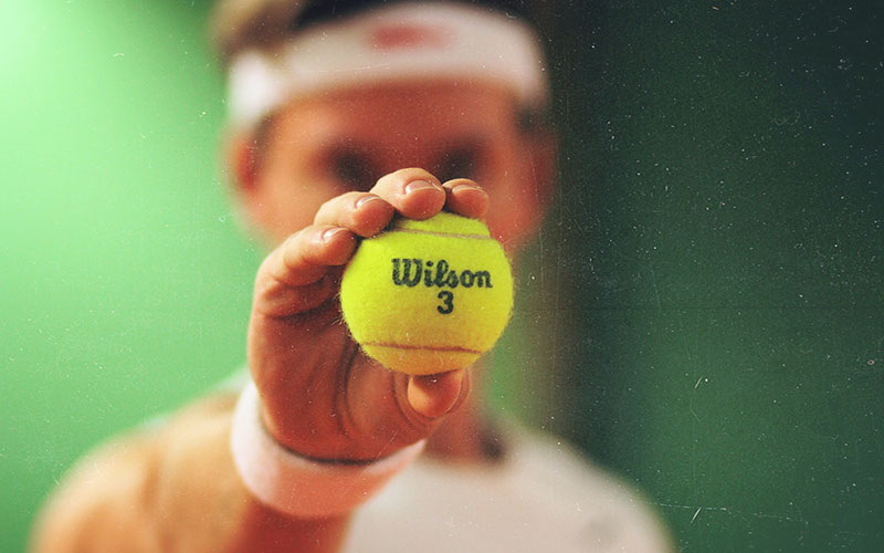 Mentally Tough Tennis Tennis player holding a Wilson 3 tennis ball, wearing a white headband and wristbands, against a green background, symbolising mental toughness in tennis.