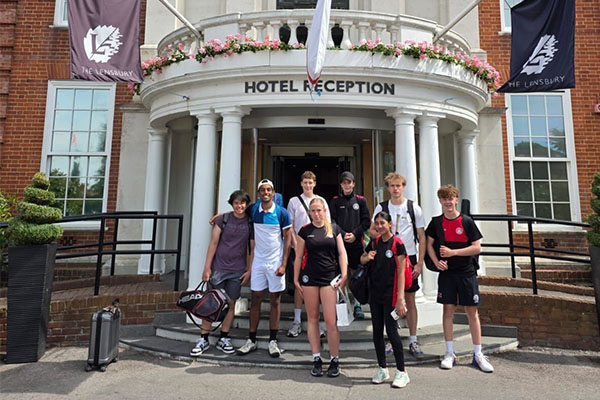Group of young tennis players posing outside The Linsbury hotel in Newcastle-under-Lyme, wearing sports gear and holding tennis bags.