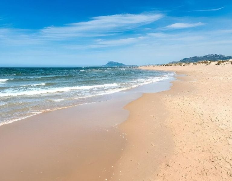 Golden sandy beach at Oliva Nova with gentle waves under a clear blue sky.