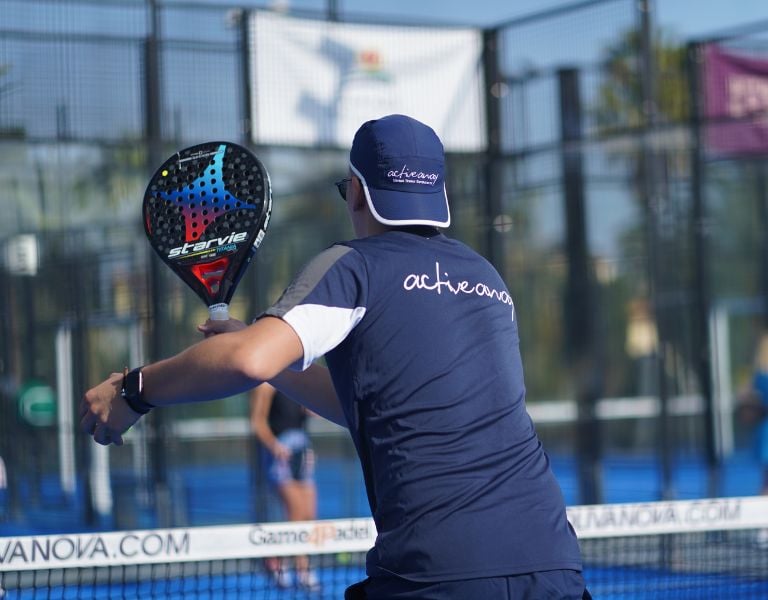 Padel coach in navy activewear branded 'active nova' on a court at Oliva Nova, holding a Startvie paddle mid-swing.