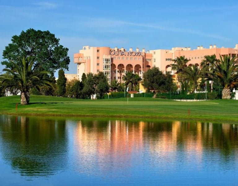 Oliva Nova Resort exterior with a golf course, palm trees, and a water feature under a blue sky.