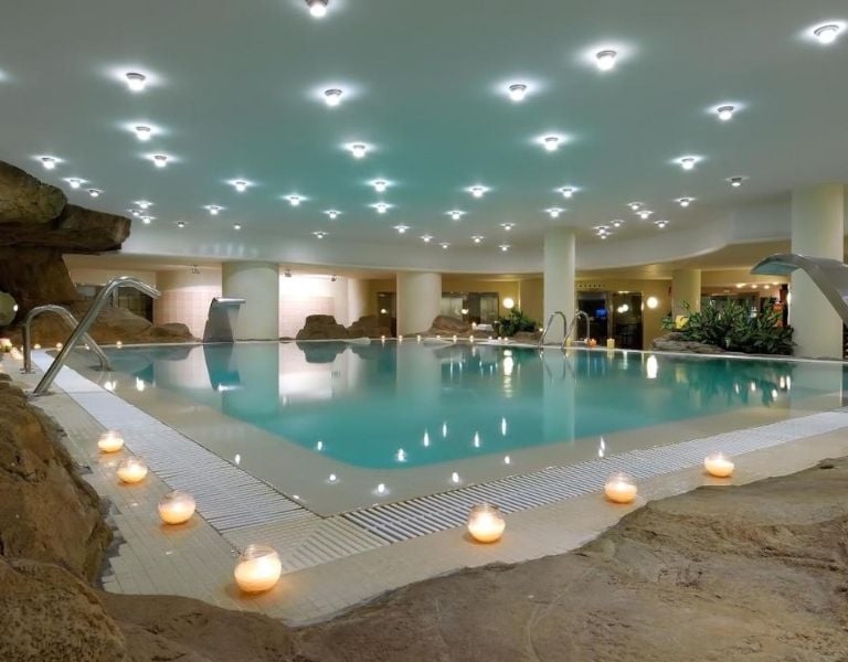 Indoor swimming pool at Oliva Nova Padel with rock formations and candle lighting for a relaxing atmosphere.
