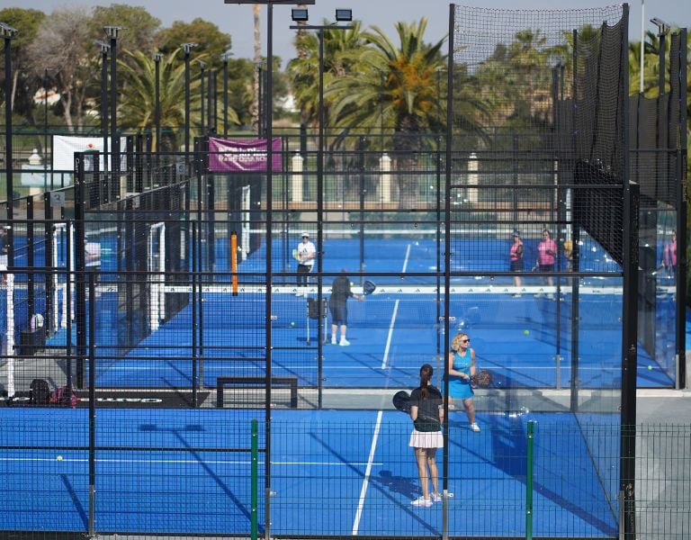 Players on a blue padel court at Oliva Nova Beach & Golf Resort, surrounded by palm trees and netted walls.