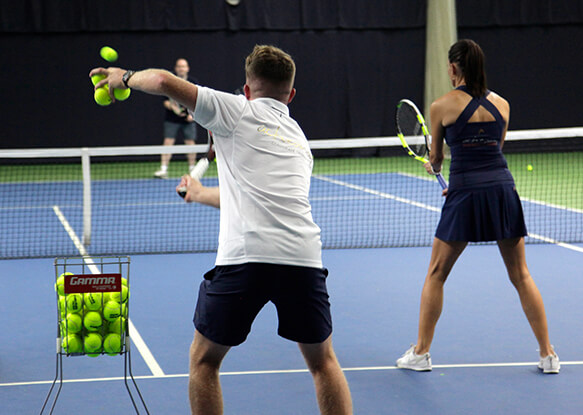 Tennis coach and female player practising serving techniques during a one-day tennis clinic on an indoor court.