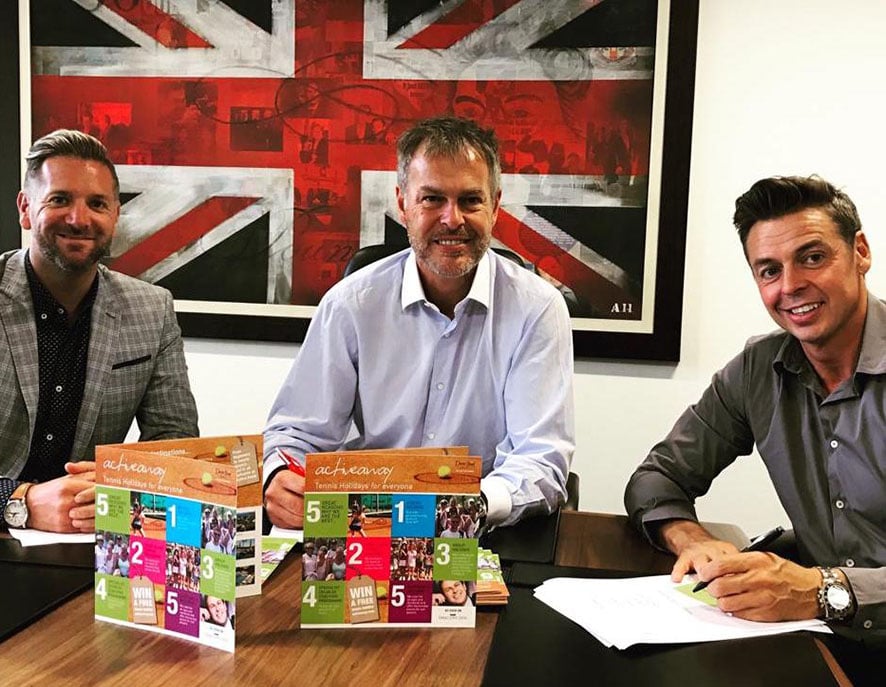 Peter Jones with two colleagues at a table discussing 'achievary' products, with a Union Jack artwork in the background.