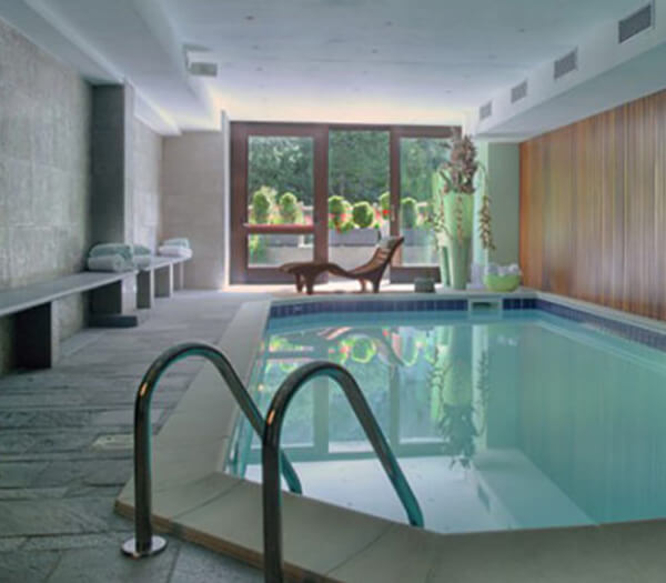 Elegant indoor swimming pool with clear water, stone tiles, large windows, and lounge chairs, offering a relaxing atmosphere.