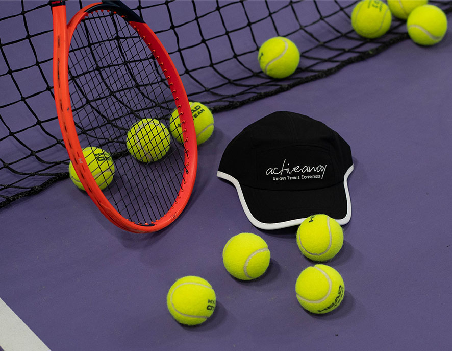 Tennis racket, several yellow balls on a purple court, and an 'Active Away Tennis Holidays' cap.