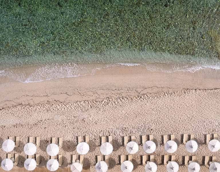 Aerial view of Royal Mare Beach featuring rows of sun loungers and white parasols, next to the turquoise sea.