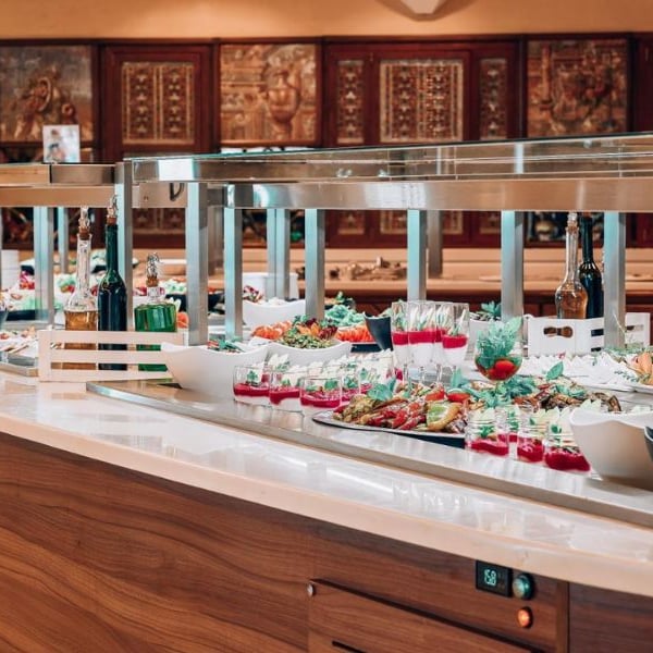Luxurious buffet at Royal Mare Gallery with gourmet dishes, salads, drinks, and elegant presentation on a wooden counter with stainless steel warming lamps.