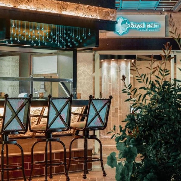 Outdoor bar at Royal Mare Gallery with stylish bar stools and Royal Palm hotel sign amidst lush greenery.