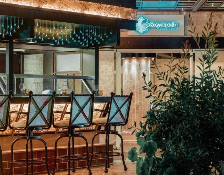 Outdoor bar at Royal Mare Gallery with stylish bar stools and Royal Palm hotel sign amidst lush greenery.
