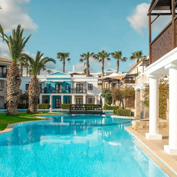 Luxurious pool at Royal Mare with palm trees and Mediterranean-style villas in the background, under a clear blue sky.