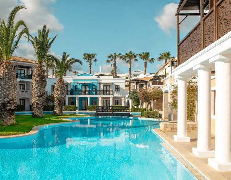 Luxurious pool at Royal Mare with palm trees and Mediterranean-style villas in the background, under a clear blue sky.