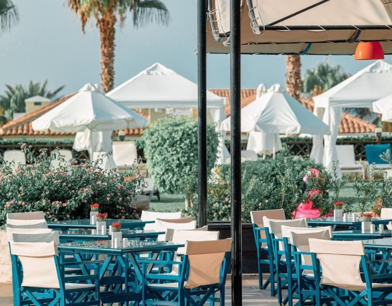 Royal Mare Gallery outdoor restaurant with blue tables and chairs, surrounded by greenery and white parasols.