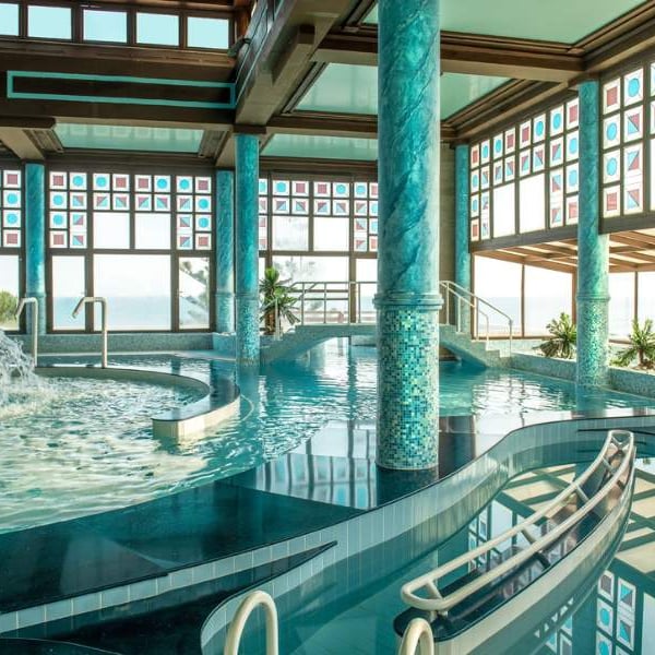 Luxurious indoor spa area at Royal Mare Gallery, featuring a large pool with mosaic columns and panoramic windows with views outside.