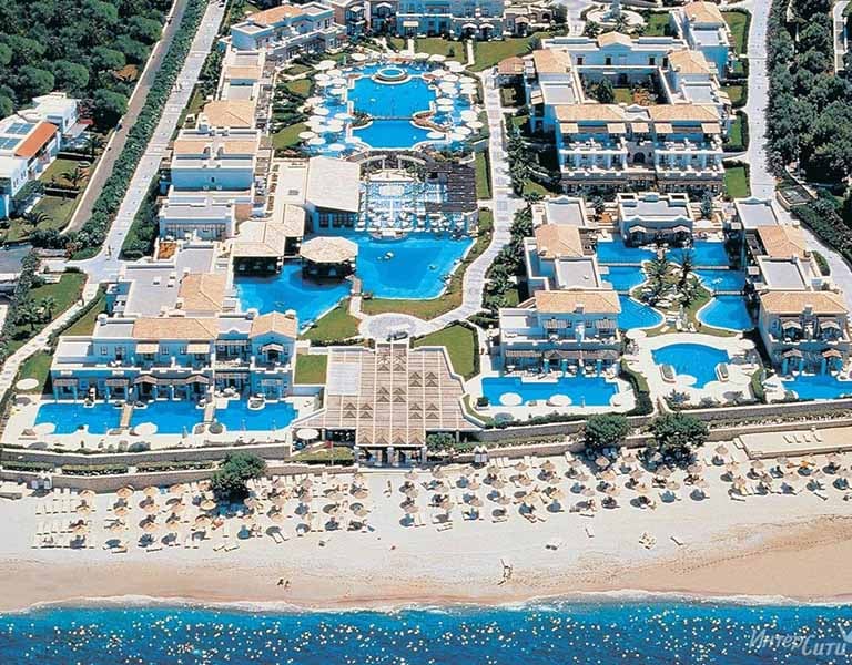 Aerial view of Aldemar Royal Mare resort in Crete, featuring multiple swimming pools, accommodation buildings, and a beachfront with loungers.