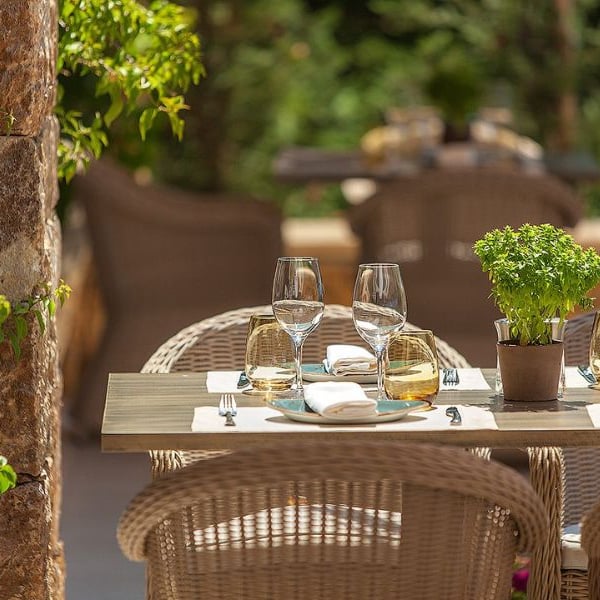 Table at Ammos Restaurant in Sani Beach with glassware, wicker chairs, and a potted herb centrepiece in an outdoor setting.