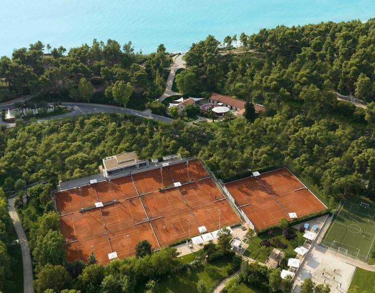 Aerial view of Sani Beach tennis courts surrounded by trees and near the Aegean Sea.