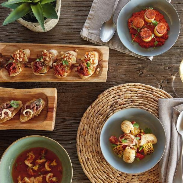 Mediterranean meal at Sani Beach with bruschetta, tomato-based dish, soup, and grilled shellfish on a rustic wooden table setting with a glass of white wine.