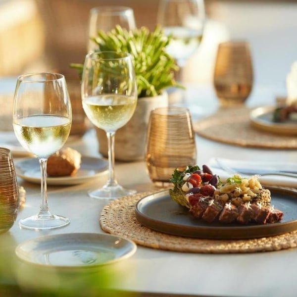 Gourmet dish with grilled meat and herbs on a table set for dining, featuring wine glasses and elegant decor at Sani Beach.