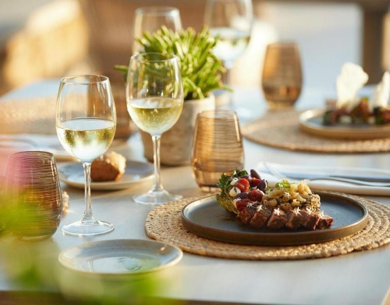 Gourmet dish with grilled meat and herbs on a table set for dining, featuring wine glasses and elegant decor at Sani Beach.